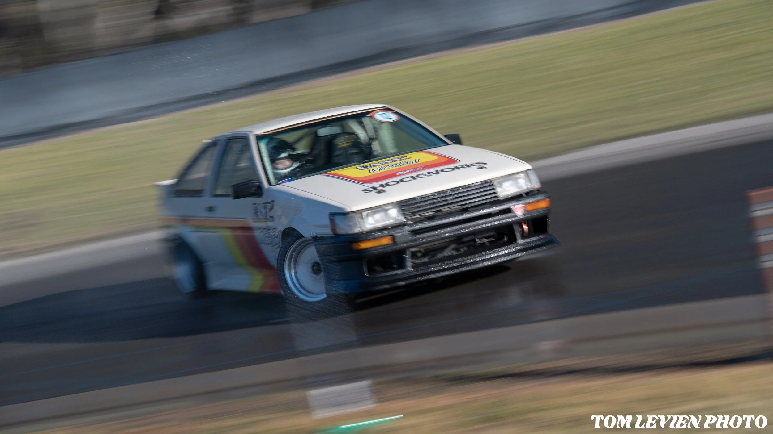 A vintage race car speeding on a race track, with motion blur indicating high speed and a driver inside wearing a helmet.