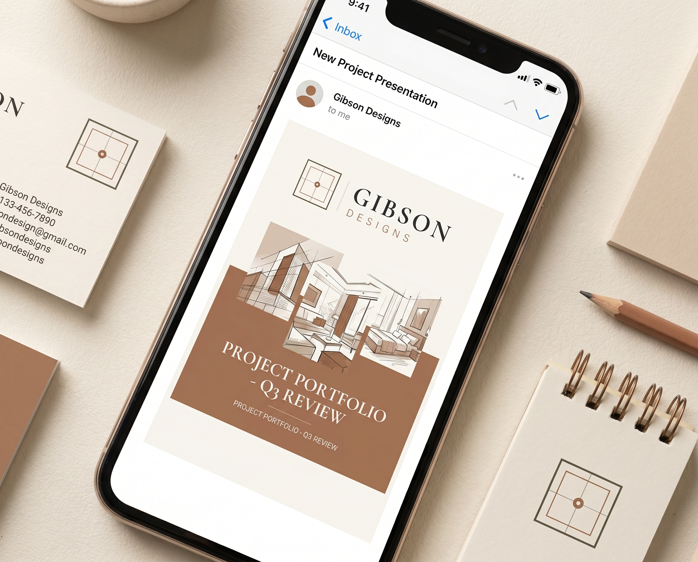 A smartphone displaying an email inbox with an email from Gibson Designs about a project portfolio review, placed on a beige desk alongside business cards, a notebook, pencils, and a cup.