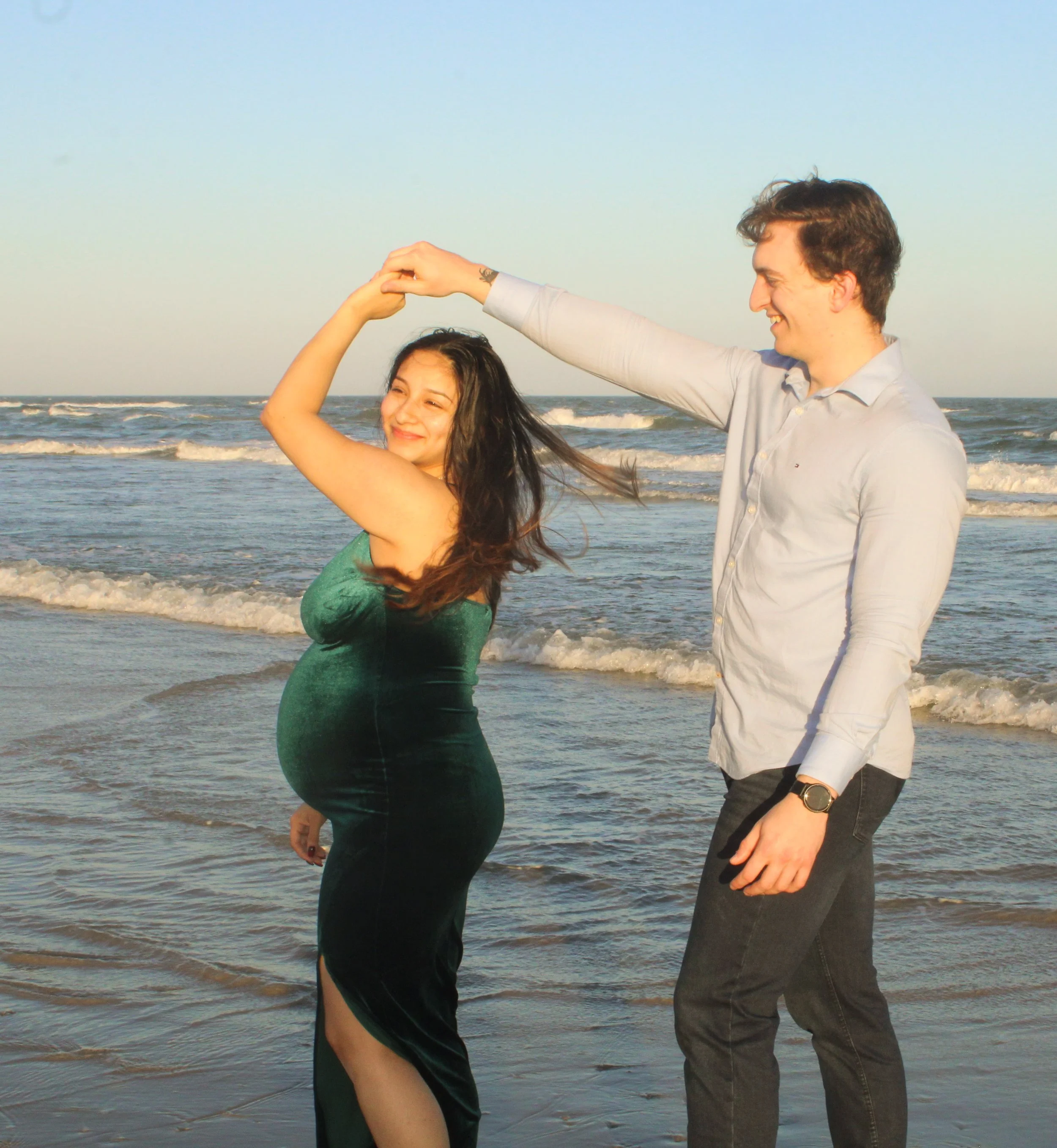A man and woman dancing on the beach with the ocean in the background during sunset.