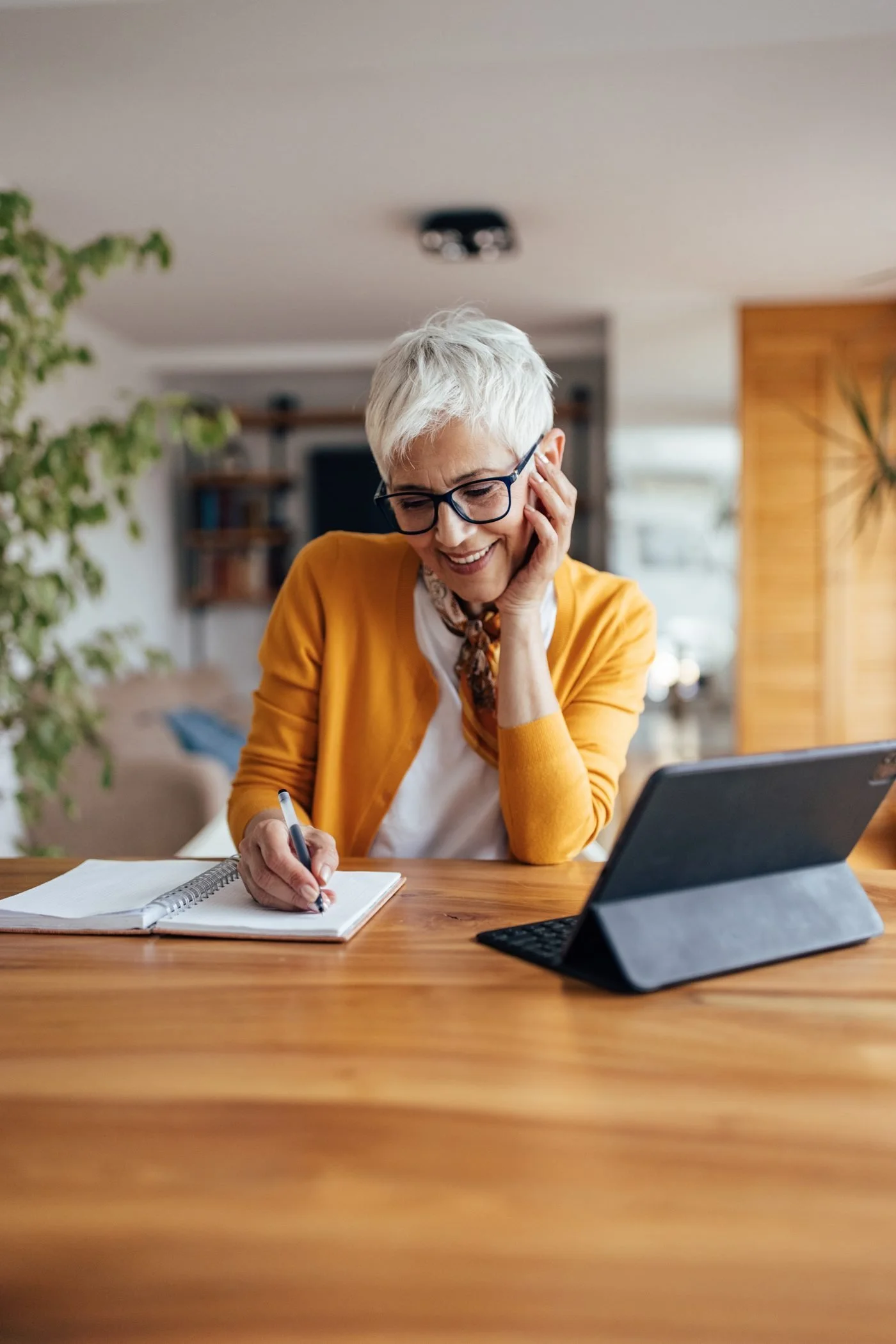 Smiling older woman on the phone at her kitchen table, reviewing her Medicare questions