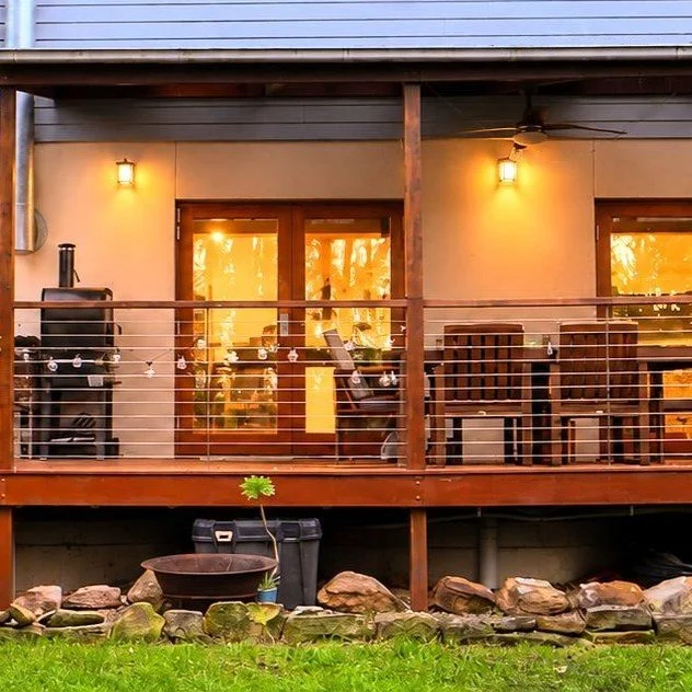 Backyard deck with outdoor furniture and string lights, illuminated by yellow wall sconces, overlooking a garden with rocks.