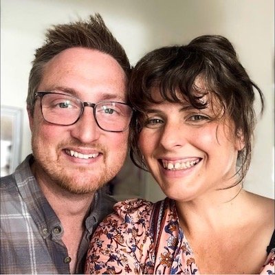 A man and a woman smiling and taking a close-up selfie indoors.
