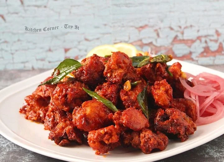 Plate of spicy Indian cauliflower fritters garnished with curry leaves and served with sliced onions and lemon wedges, on a white oval dish.