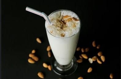 A tall glass of iced coffee with a straw, topped with whipped cream and caramel syrup, surrounded by scattered peanuts on a dark surface.