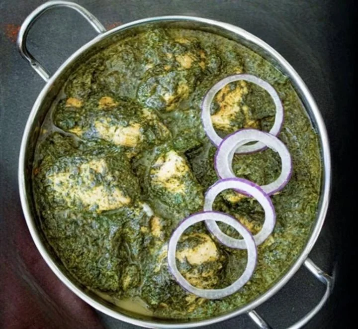 A pot containing fish curry with onion rings on top.