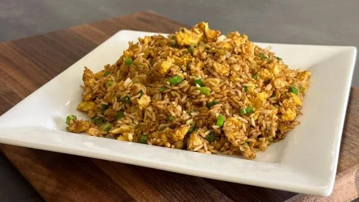 A plate of fried rice with scrambled eggs and chopped green onions on a white square dish, placed on a wooden surface.
