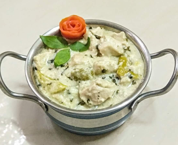 Creamy chicken and vegetable curry garnished with a carved tomato rose and basil leaves in a small metal bowl.
