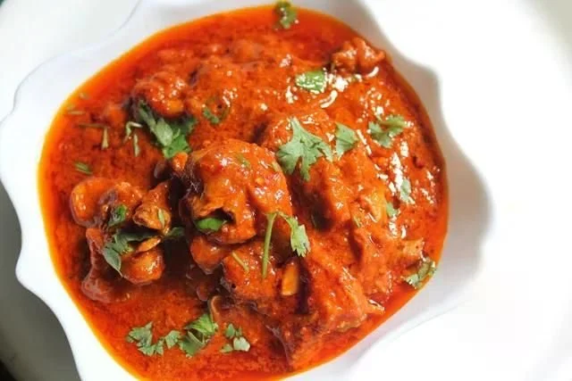 A bowl of Indian chicken curry garnished with cilantro leaves.