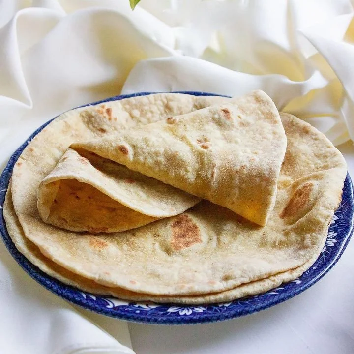 Three pieces of flatbread on a blue decorative plate, with one piece folded over, resting on a white fabric background.