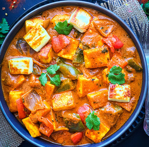 Vegetarian curry with paneer cheese, bell peppers, and tomatoes garnished with cilantro, served in a black bowl.
