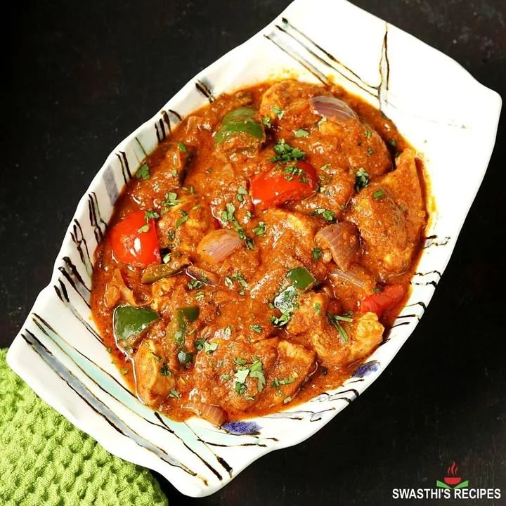 A bowl of Indian chicken curry with tomatoes, onions, and spices, garnished with chopped cilantro, in an oval decorative dish.