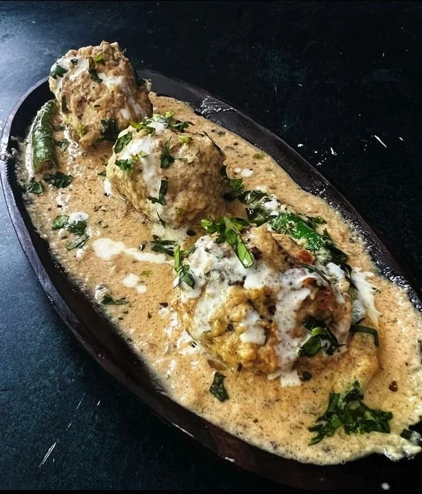 Three large meatballs in a creamy sauce garnished with chopped herbs on a black dish.