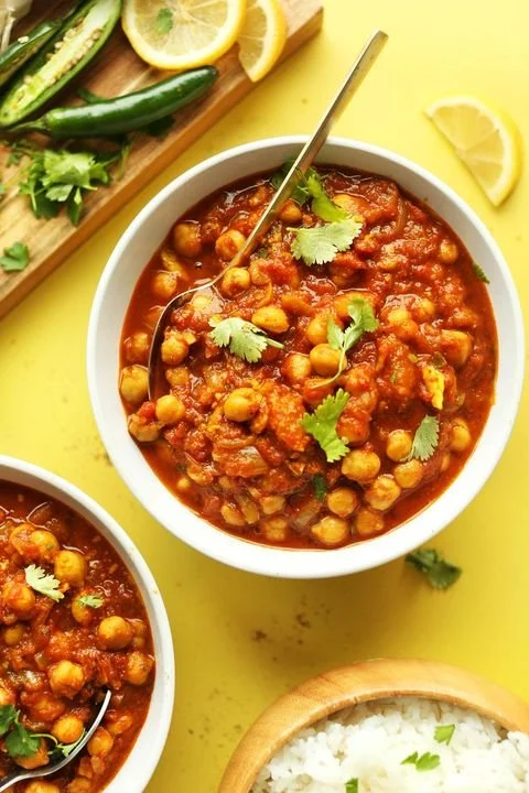 Chickpea curry with cilantro garnish, lemon slices, cucumber, and rice on a yellow background.