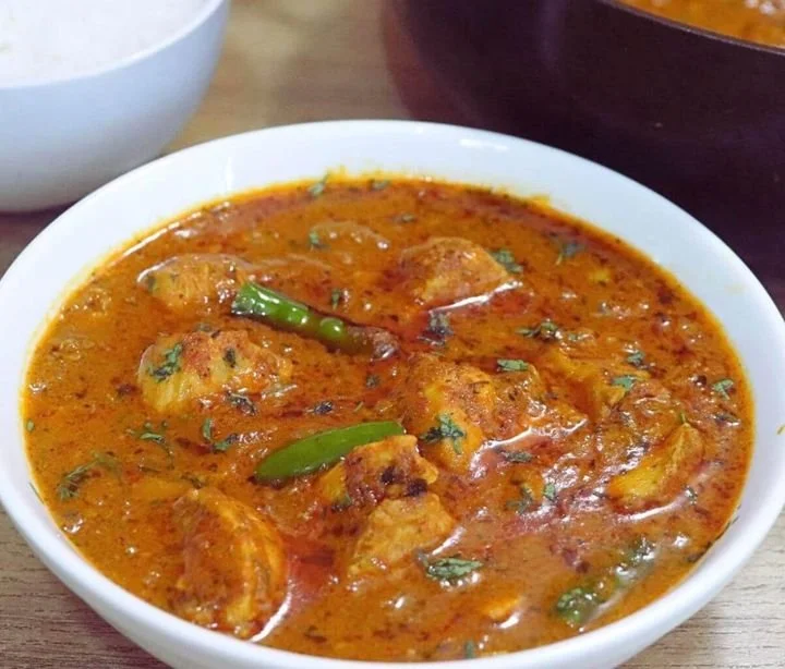A bowl of Indian chicken curry with green chili slices and herbs, served in a white bowl.