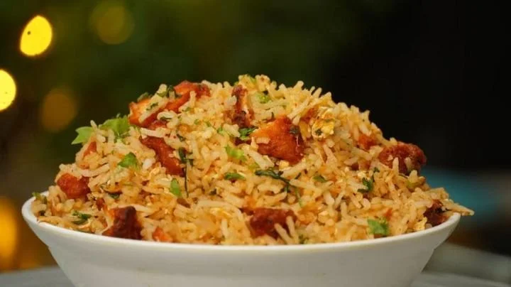 A bowl of fried rice with pieces of chicken and chopped green onions.