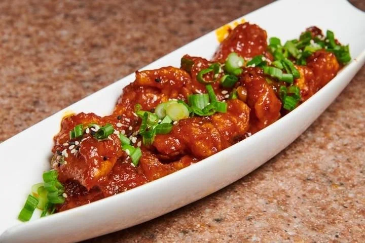 Sweet and sour chicken garnished with chopped green onions on a white, boat-shaped plate