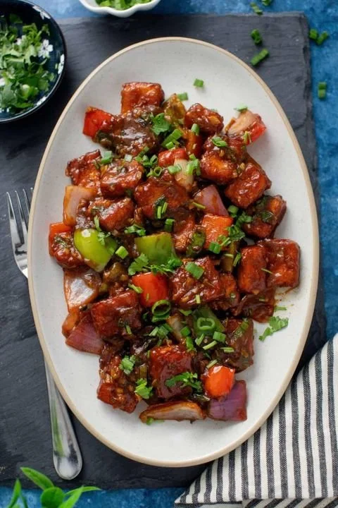 Sweet and sour pork with chunks of pork, red and green bell peppers, onions, and chopped green onions on an oval plate