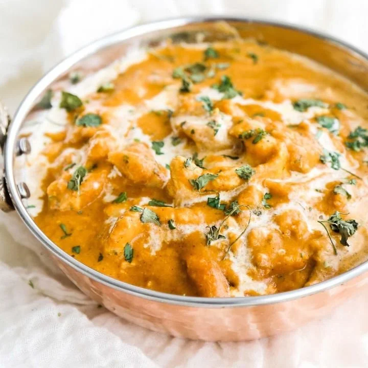A pot of chicken curry garnished with chopped cilantro, showing a creamy orange sauce and pieces of chicken.