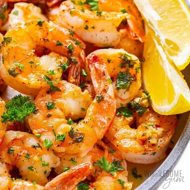 Close-up of cooked shrimp garnished with chopped parsley and lemon wedges.