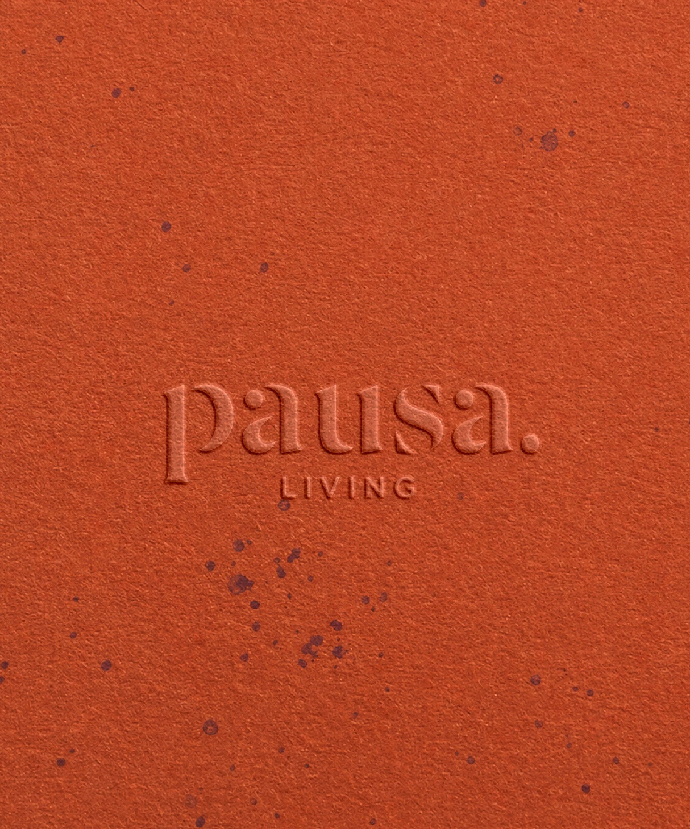 A close-up of an orange textured surface with small purple paint splatters and the word 'paisa' embossed in lowercase letters.