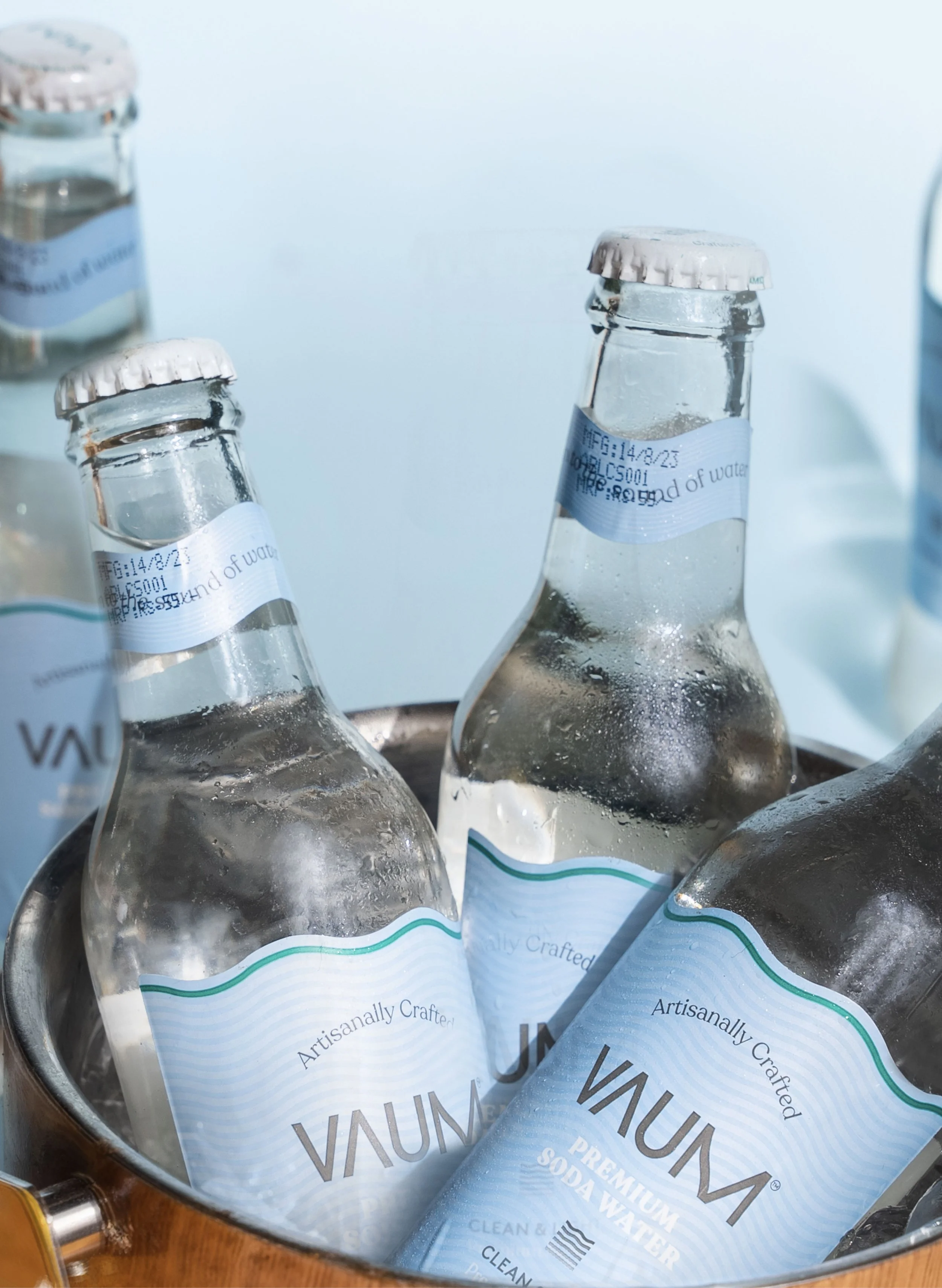 Several glass bottles of AVU Premium Soda Water inside a metal bucket, condensation on the bottles, labels reading 'Artisanally Crafted' and 'Premium Soda Water'.