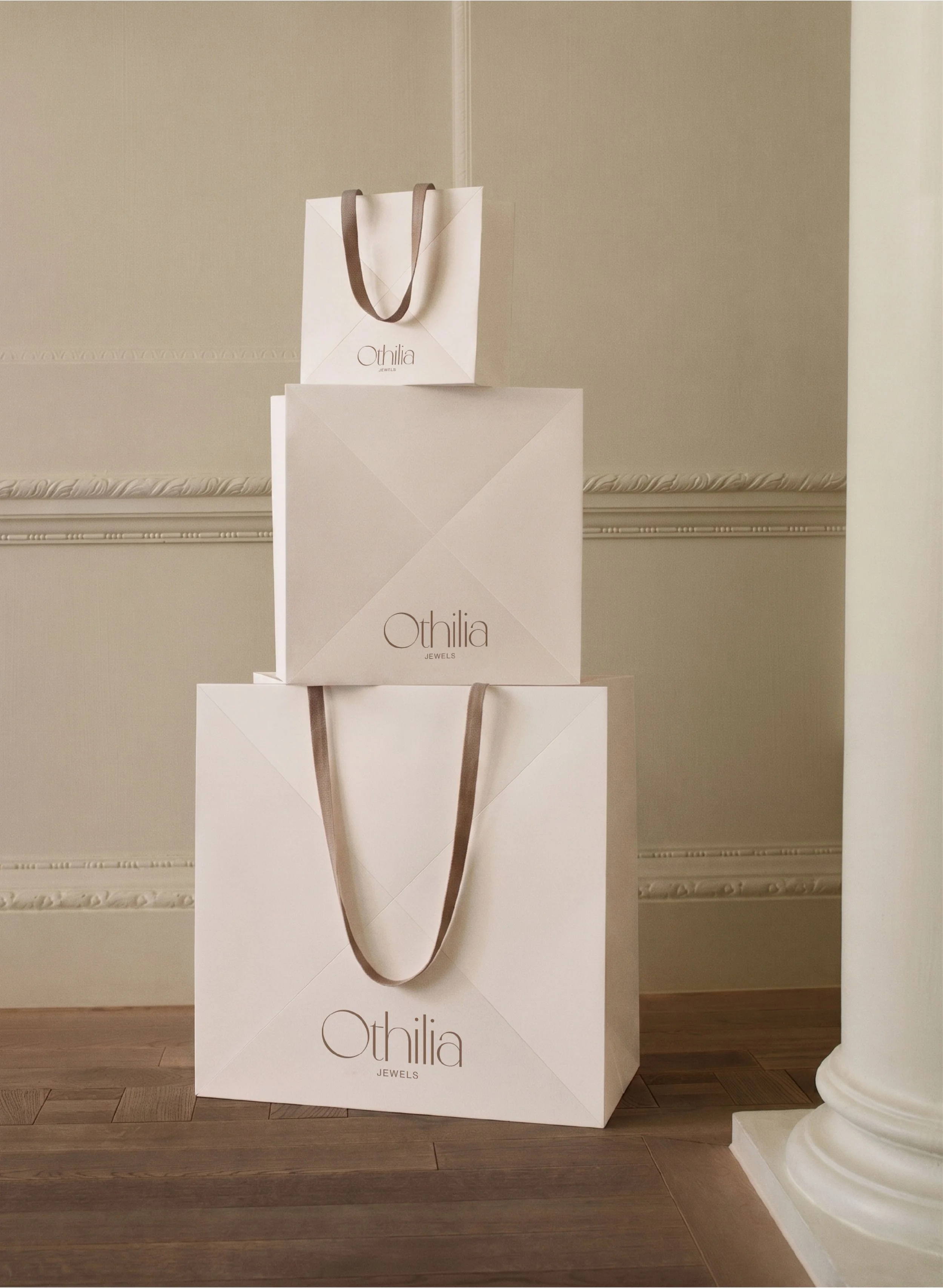 A display of white shopping boxes with the brand name 'Othilia Jewels' in a room with wooden floors and ornate wall molding, one of which contains a shopping bag with brown handles.