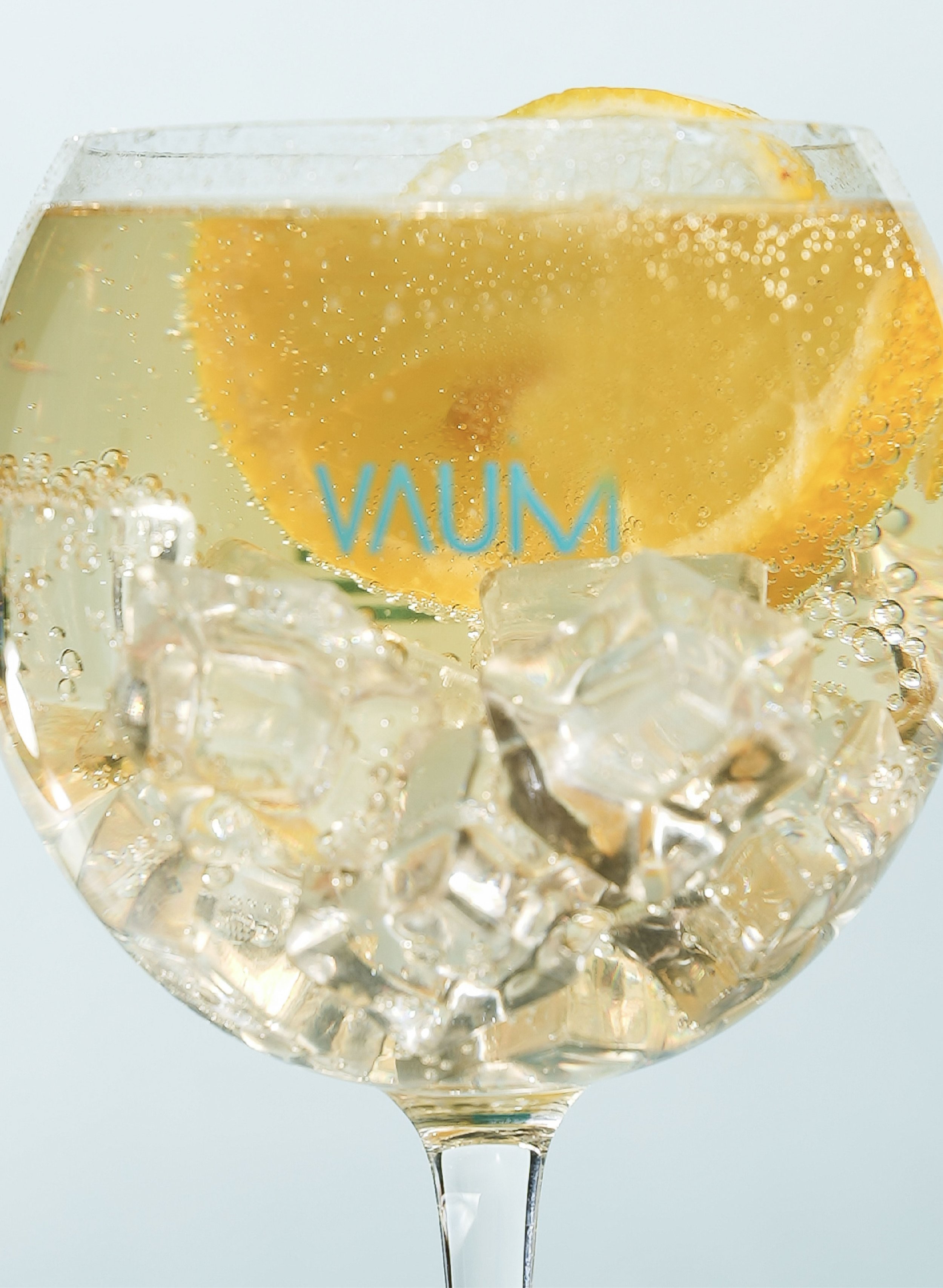 A glass of sparkling wine with lemon slices and ice cubes, with the word VAUM on the glass.