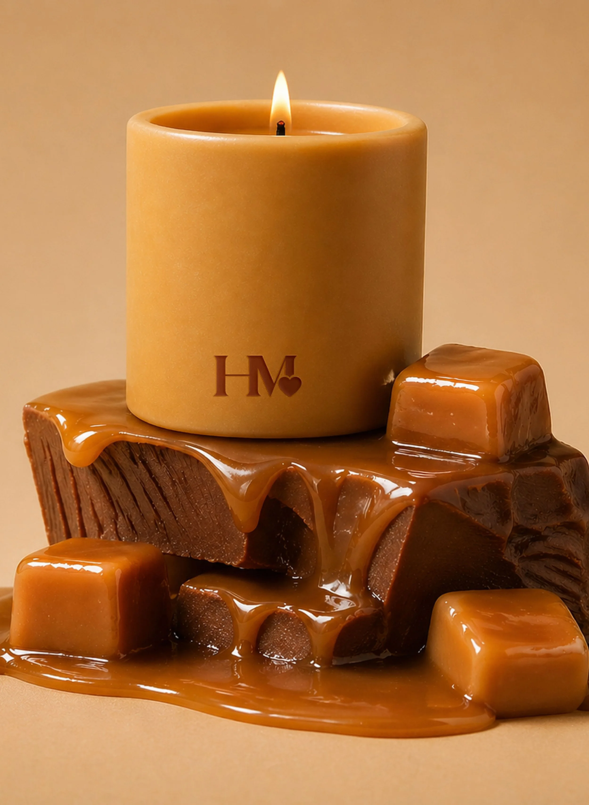 A large beige candle with initials 'HM' and a small heart, surrounded by melting caramel candies and caramel sauce on a wooden surface against a warm background.