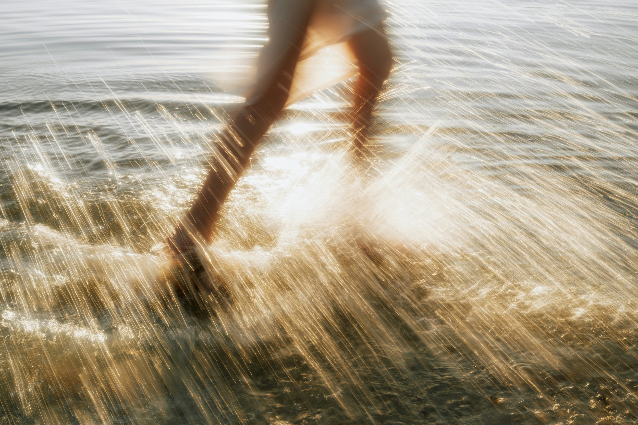 Close-up of a person's legs and feet in water with sunlight reflections and motion blur.