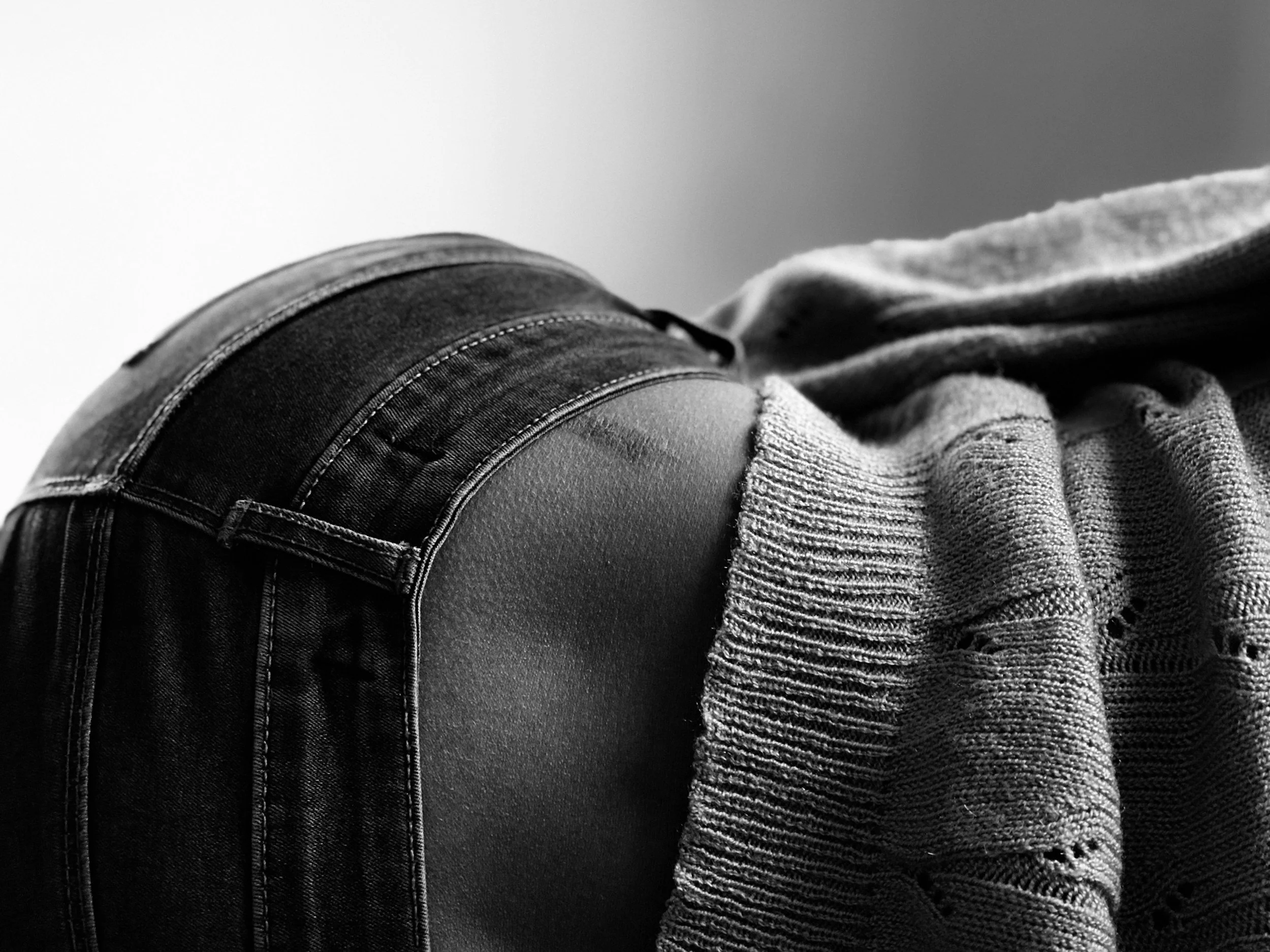 Black and white photograph of a person lying down wearing a denim jacket and a knitted sweater, with a clear sky in the background.