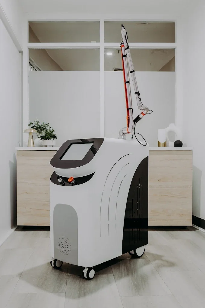 Medical or cosmetic laser treatment machine in a clean room with minimal decor, featuring a touchscreen interface and an extendable arm.