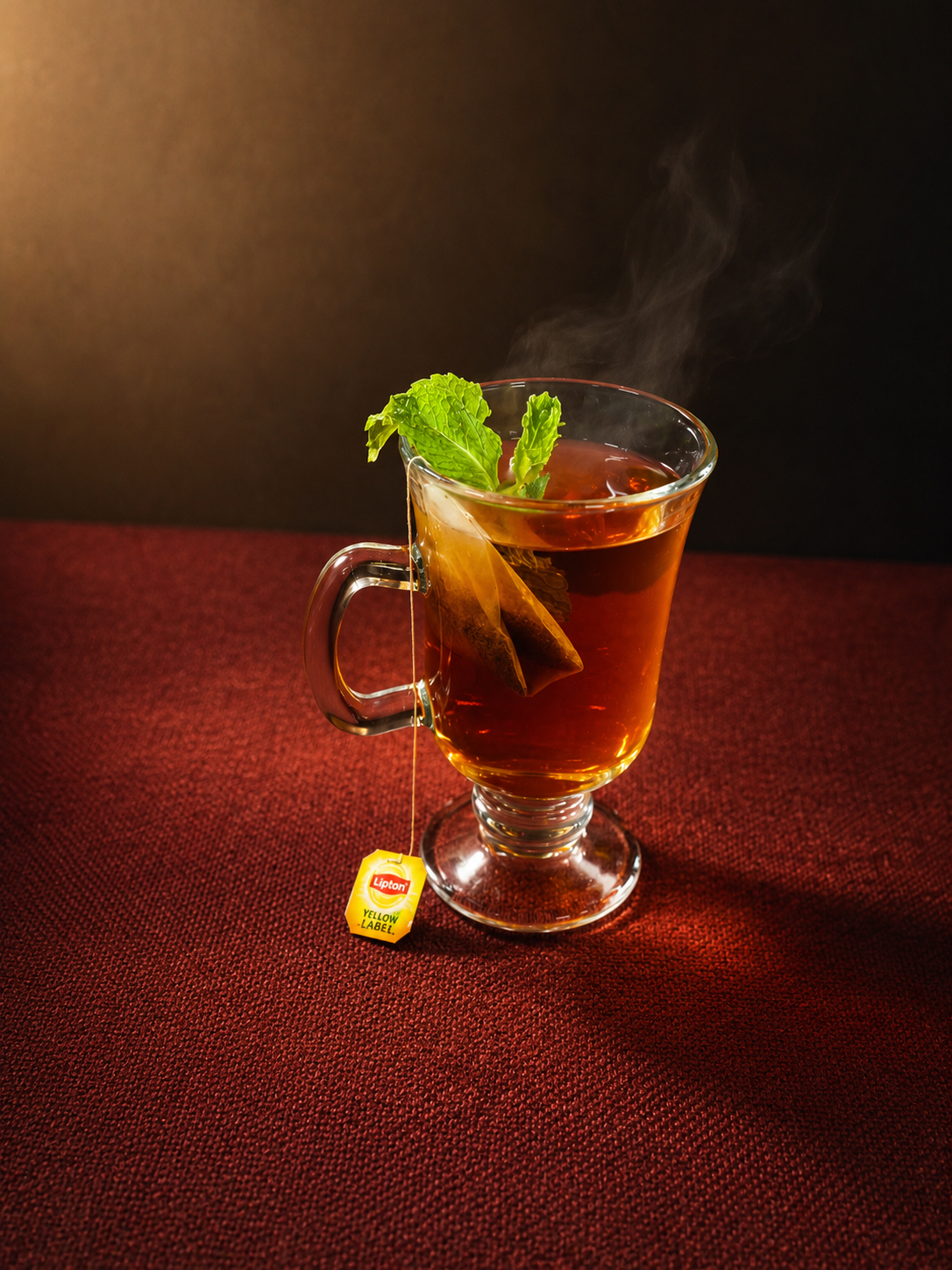 A hot cup of tea with fresh mint leaves and a tea bag, sitting on a red textured surface.