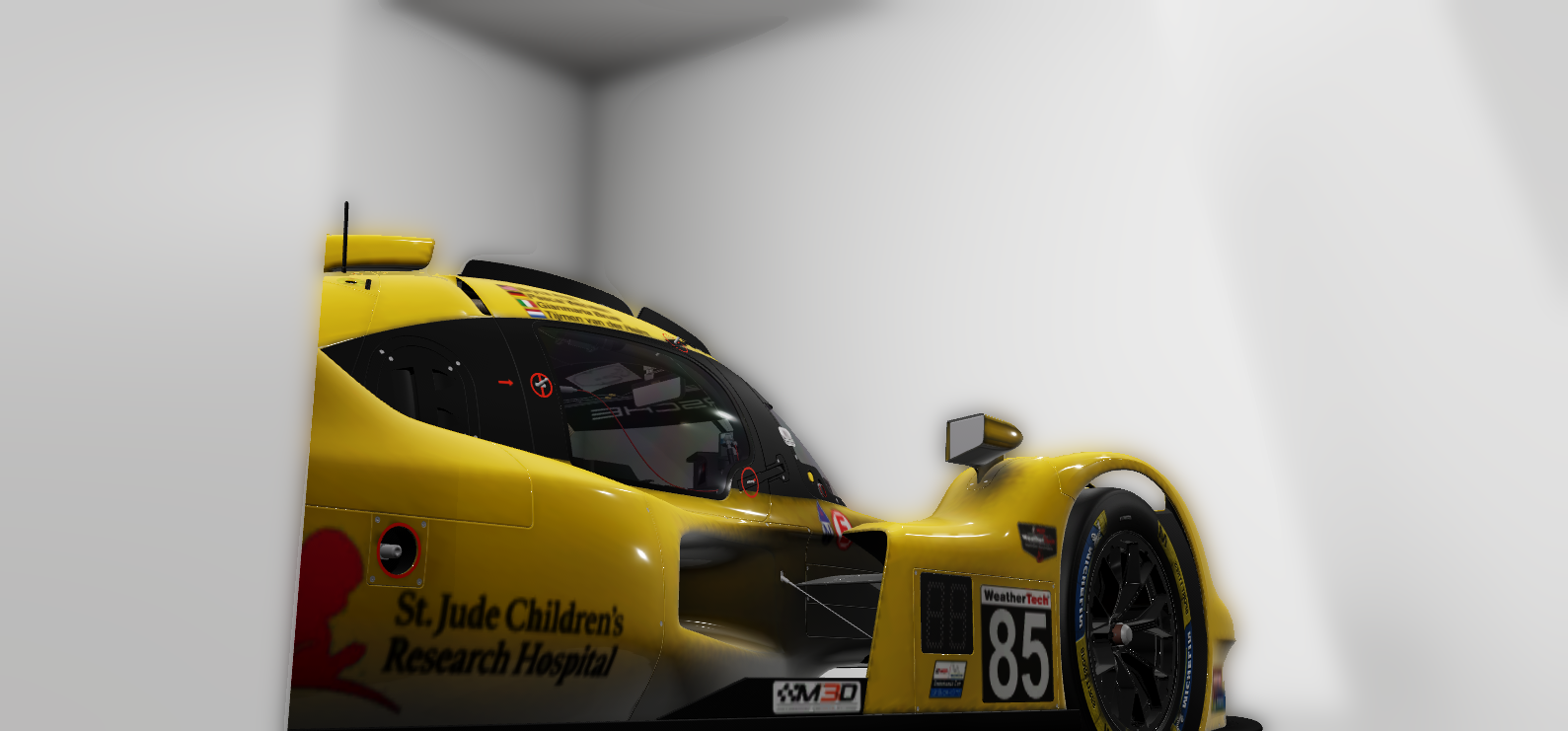 A yellow race car with black accents parked in a white room, viewed from the side with part of the front and side visible. The car has the number 85 and sponsors including "St. Jude Children's Research Hospital" on the side.