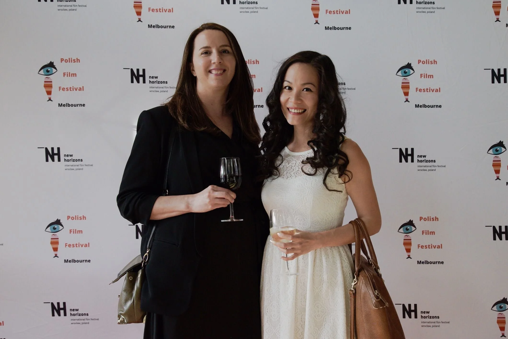 Two women standing close together and smiling at an event at the Polish Film Festival in Melbourne, with a backdrop featuring festival logos and text.