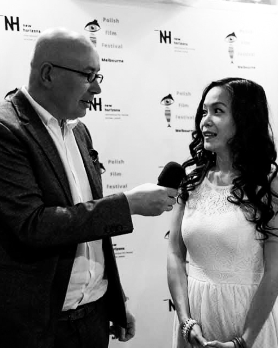 An interview taking place at the Polish Film Festival in Melbourne, with a woman in a white dress speaking into a microphone held by a man in glasses and a suit.