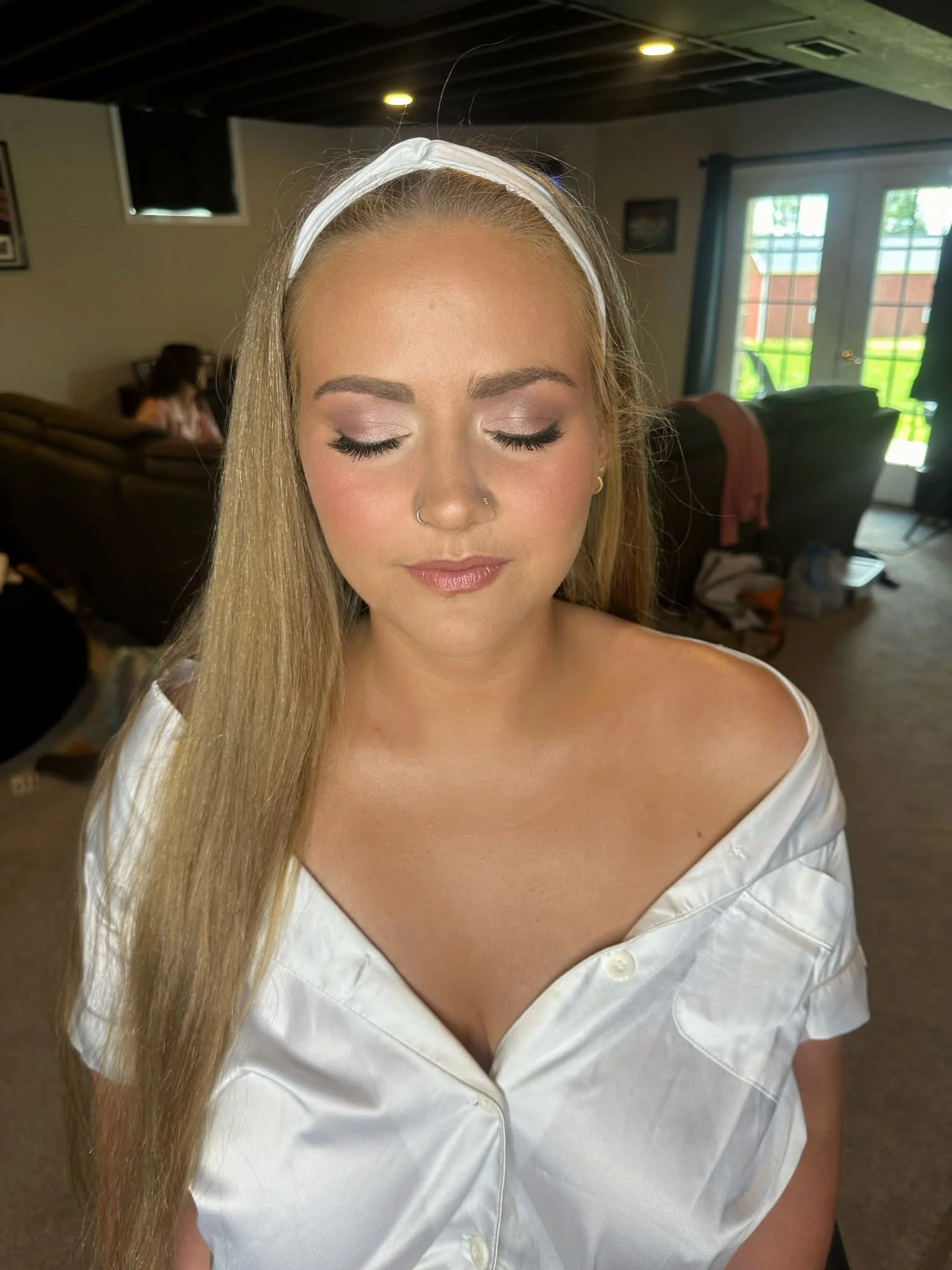 Close-up of a woman with long blonde hair, wearing a white headband and white shirt, with her eyes closed.