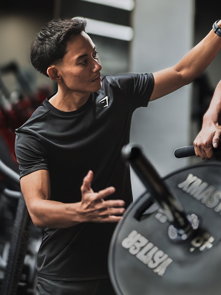 A woman in a black athletic shirt is lifting a weight plate at the gym.