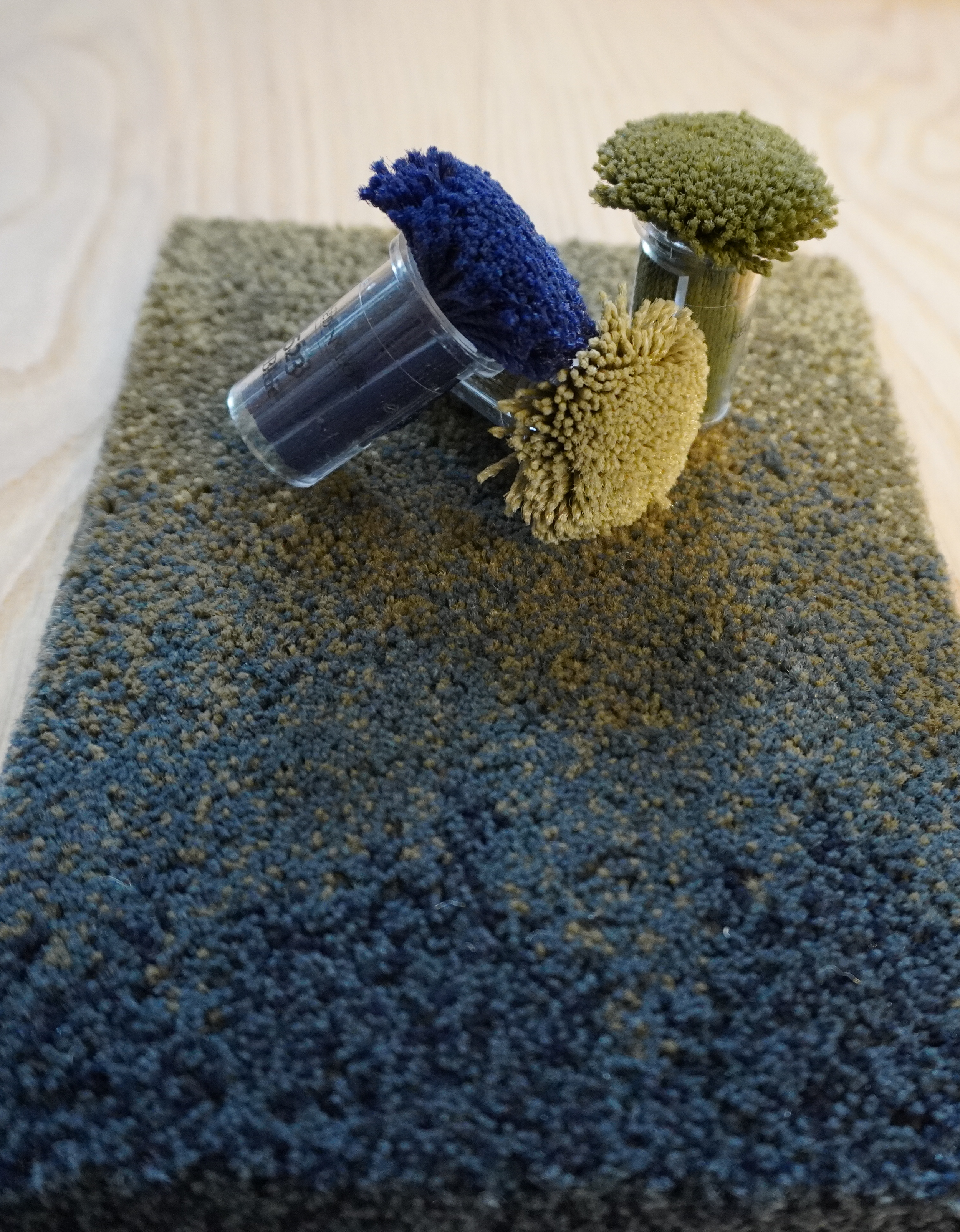 Zwei Proben von schwarzem und grünerem Bimsstein in transparenten Röhrchen auf grauem Sand.