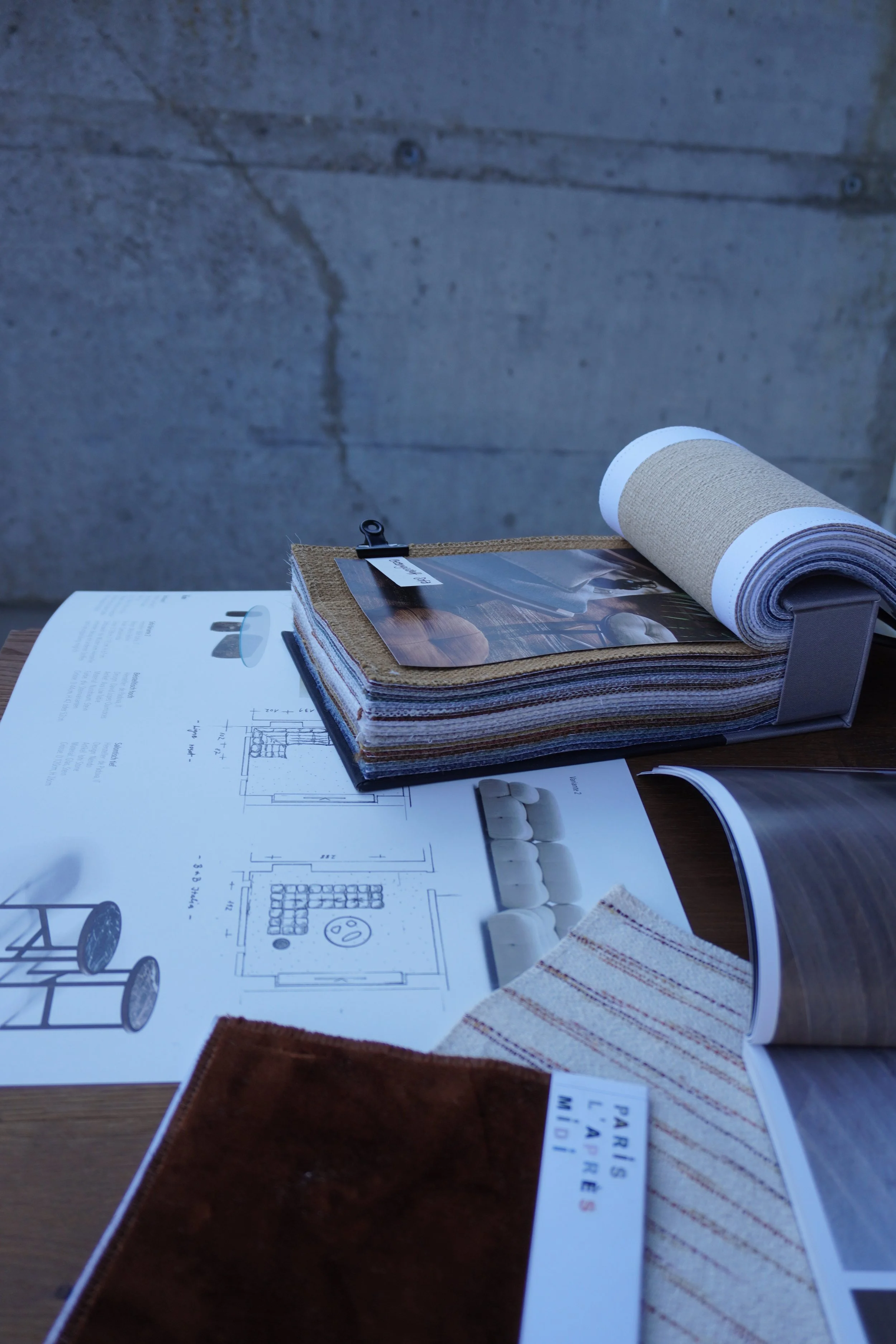 Bau- oder Architekturfotos und Materialmuster auf einem Tisch, inklusive Farbkarten und Textblättern, vermutlich für Innenarchitektur oder Renovierungsplanung.