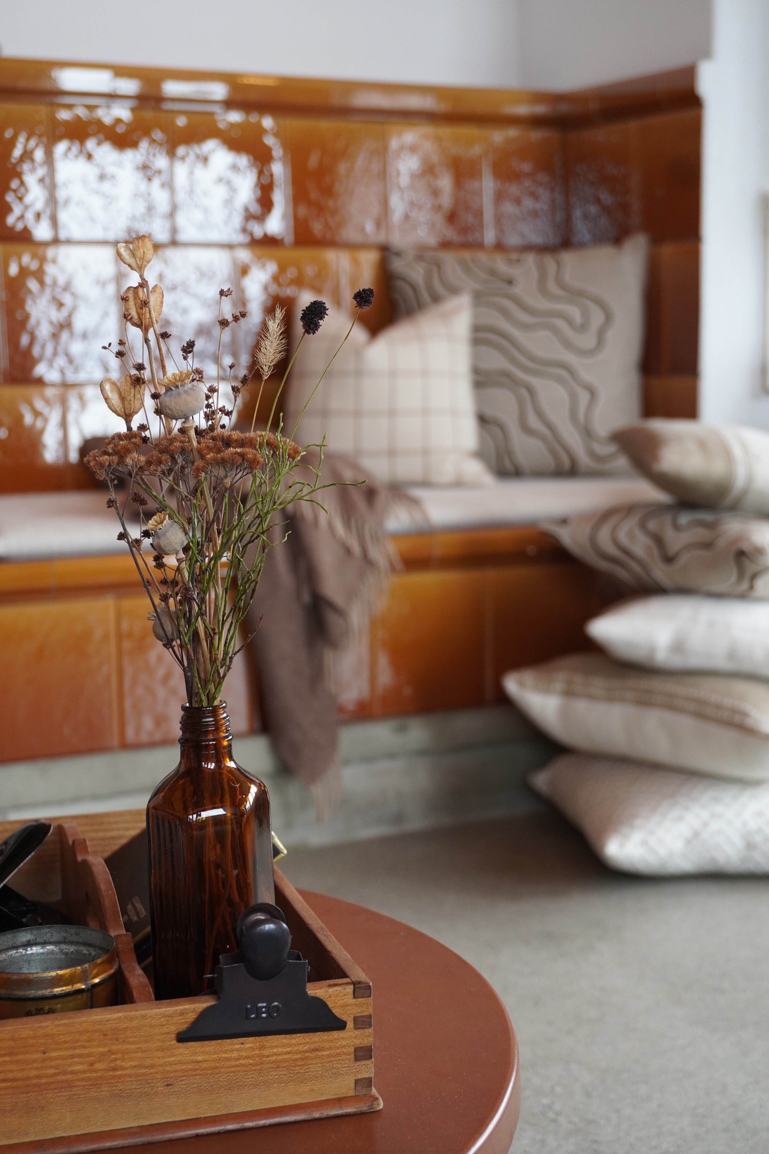 Deko-Blumen auf einem braunen Glas in einem Wohnzimmer mit Couch und Kissen im Hintergrund.