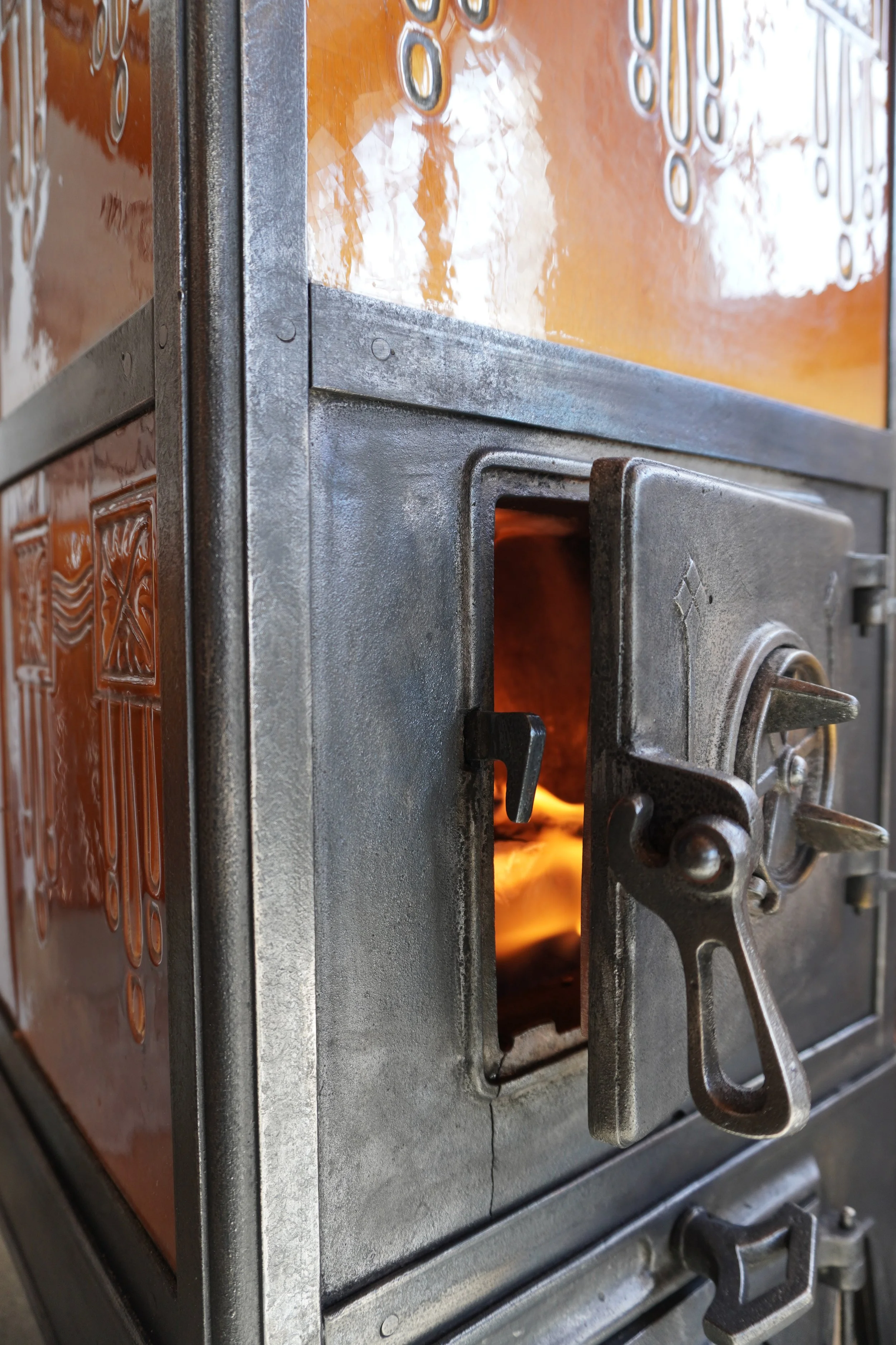 Eine alte, industriell aussehende Feuerbox mit offenem Tür und Flamme im Inneren, bestehend aus Metall und Backstein mit sichtbaren Schrauben und Griffen.