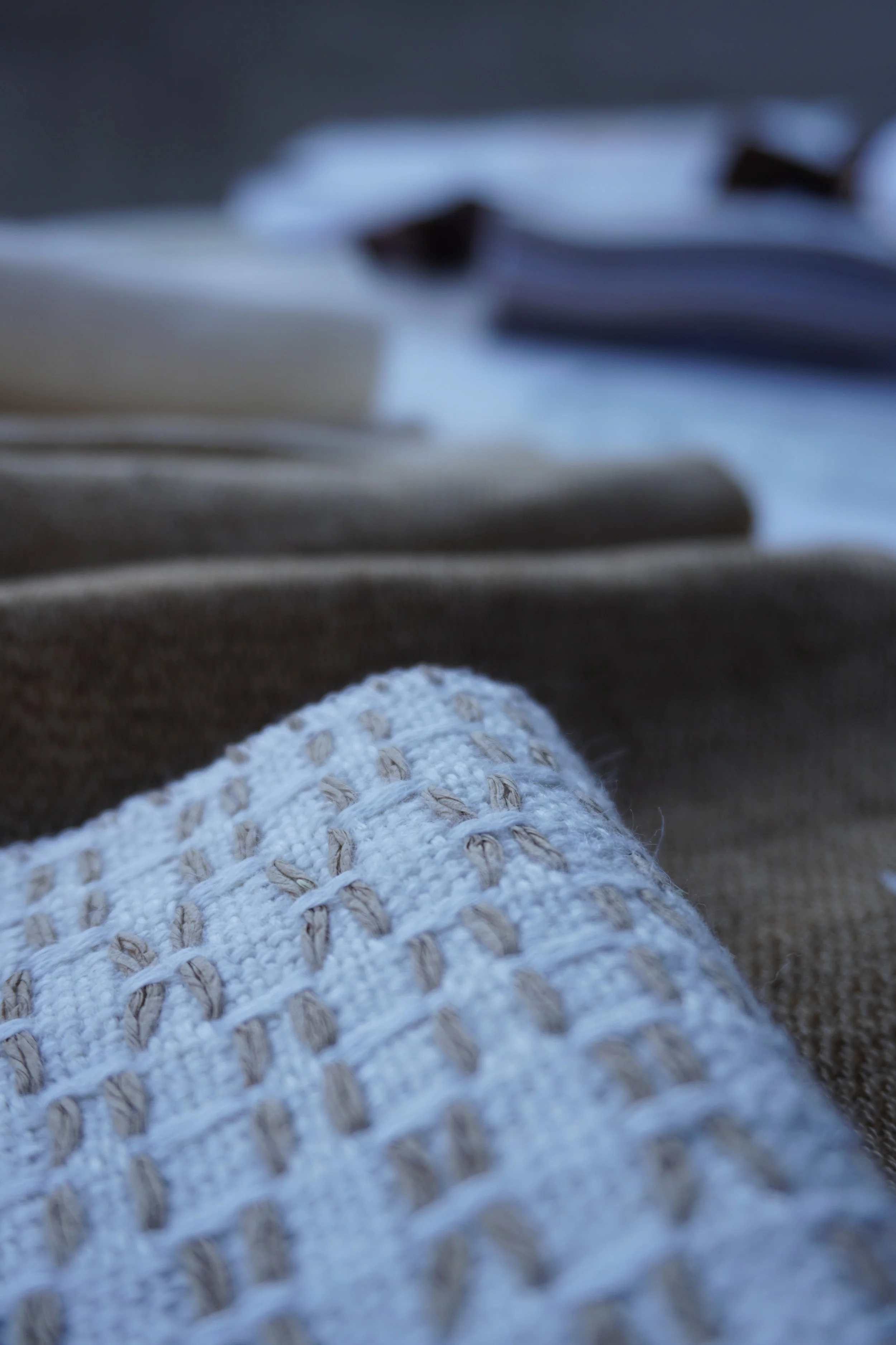 Nahaufnahme eines gestrickten Handschuhs, im Hintergrund sind ausgeblichene Baumwoll- oder Wollstoffe, alles in gedeckten Tönen.