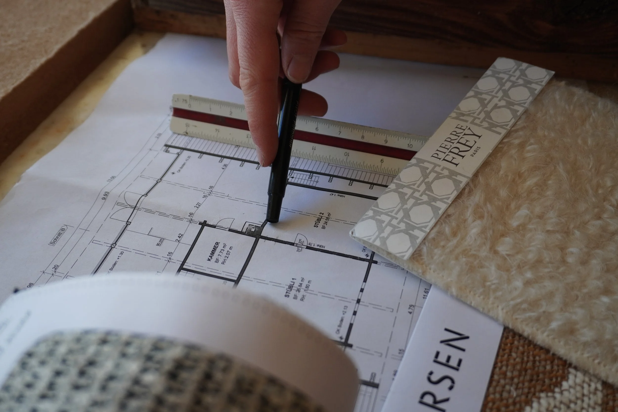 Ausdruck eines Bauplans mit Messwerkzeug und einem Menschen, der einen Stift benutzt, um den Plan zu markieren, auf einer Arbeitsfläche.