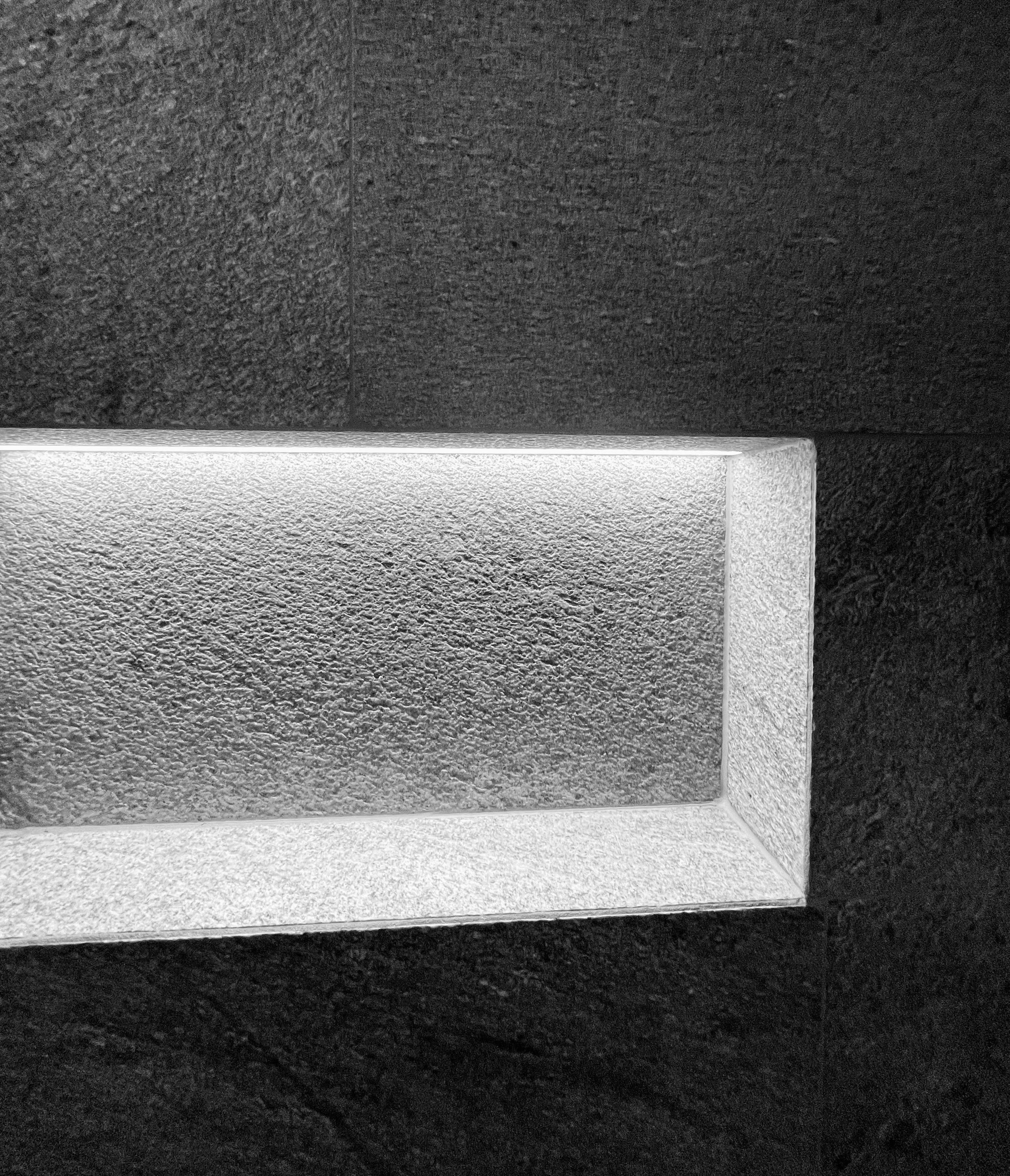 Schwarz und weißes Mosaikmuster auf einer Wand mit einem weißen Sockel. Der Boden besteht aus schwarzem Granit. Es sieht aus wie im Inneren eines modernen Gebäudes.