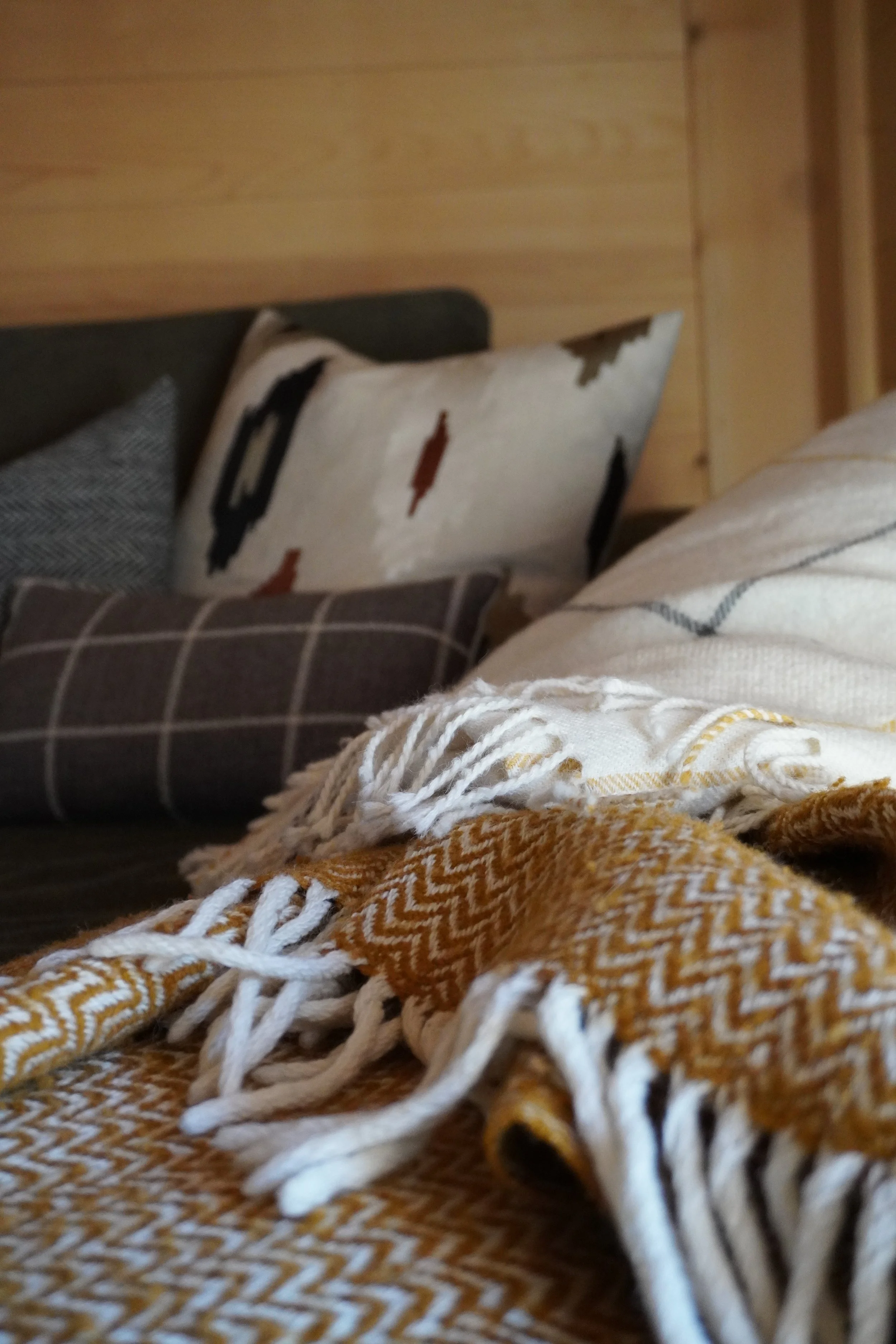 Blick auf eine gestrickte Decke und Kissen auf einem Sofa, mit Holzpaneelen im Hintergrund.