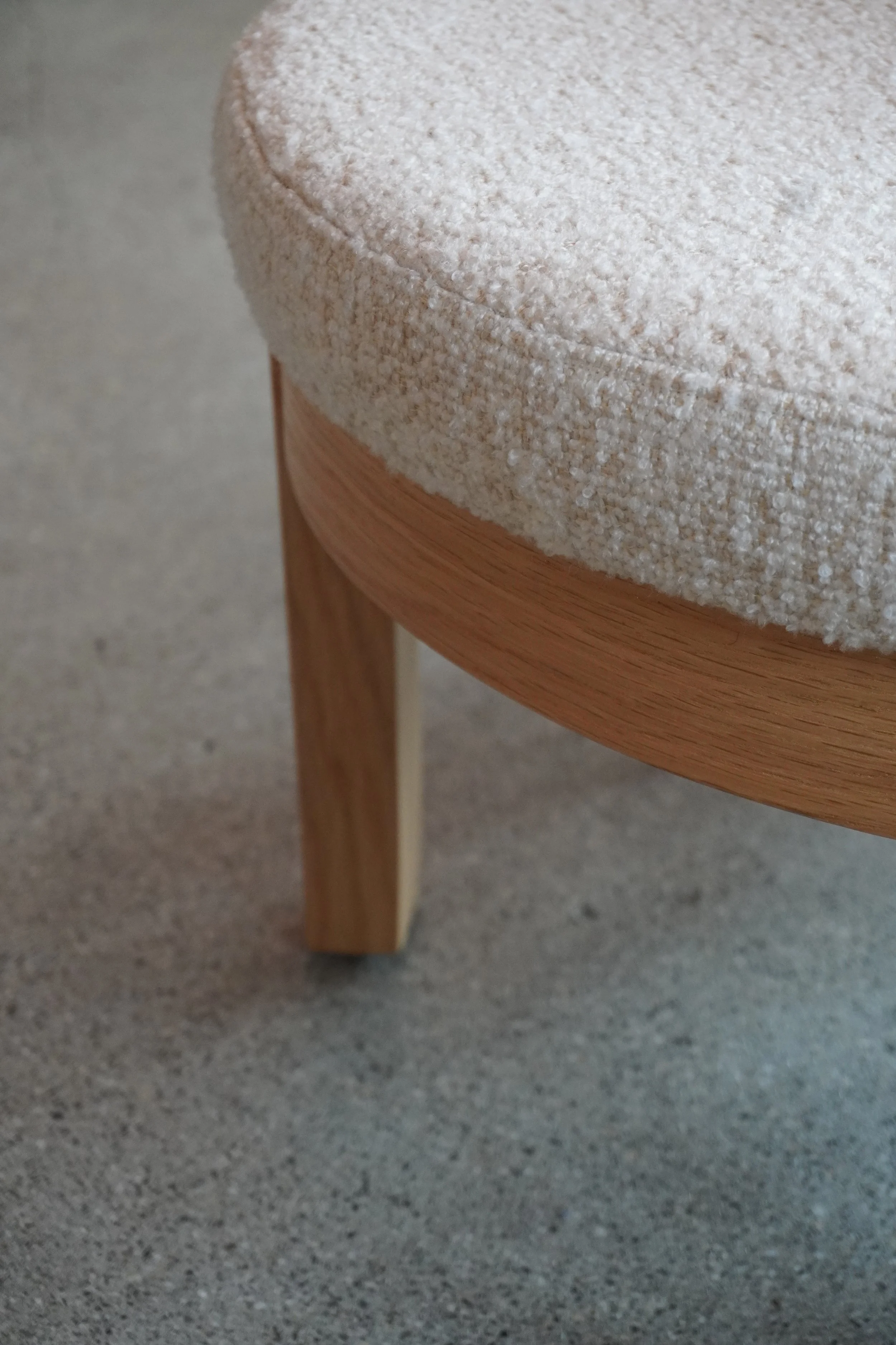 Ein Stuhl mit Holzbeinen und einem gepolsterten Sitz, die Polsterung ist beige und textured.