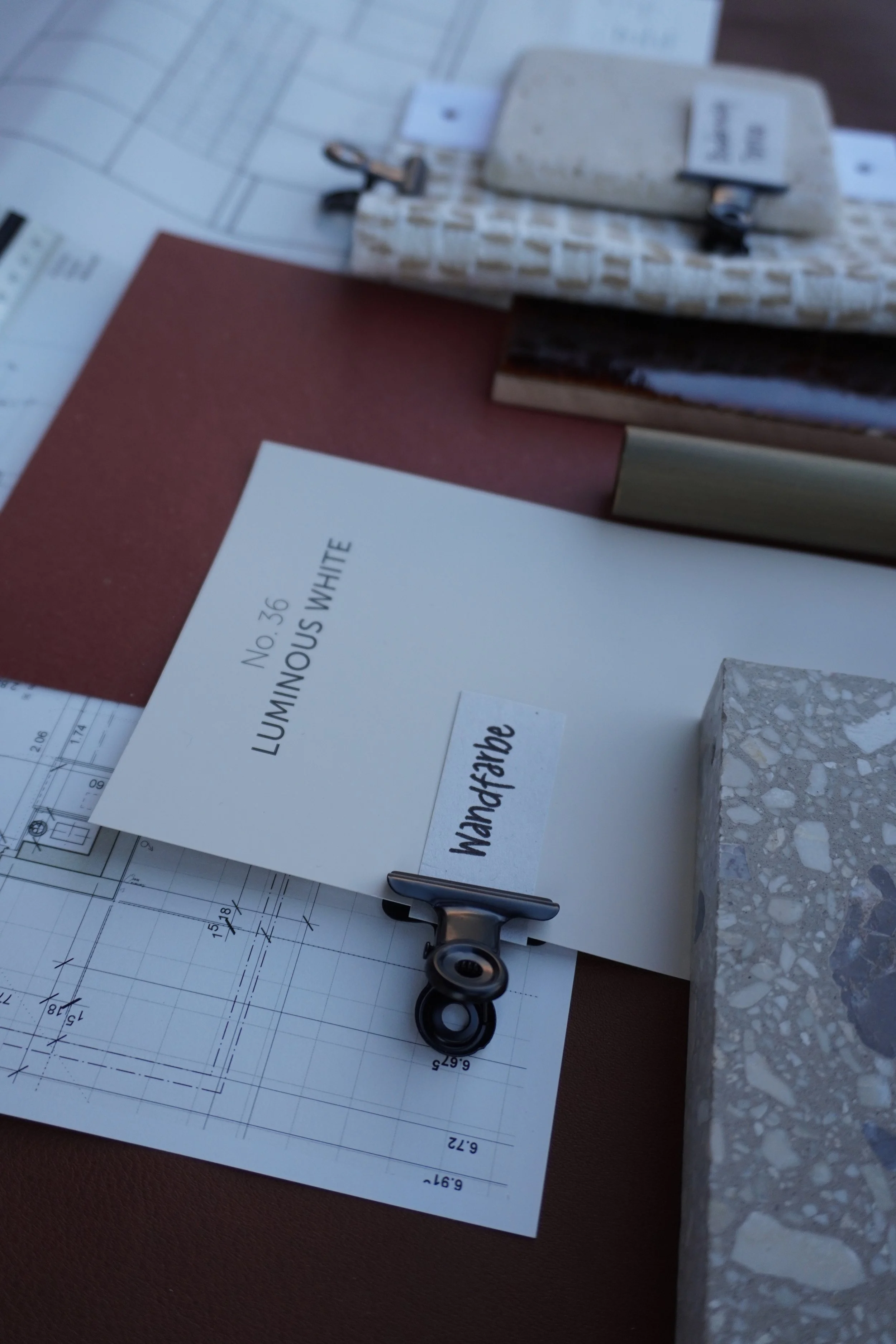 Architektenzeichnungen und Baupläne auf einem Tisch, neben Klammern und Baustoff-Probematerialien.