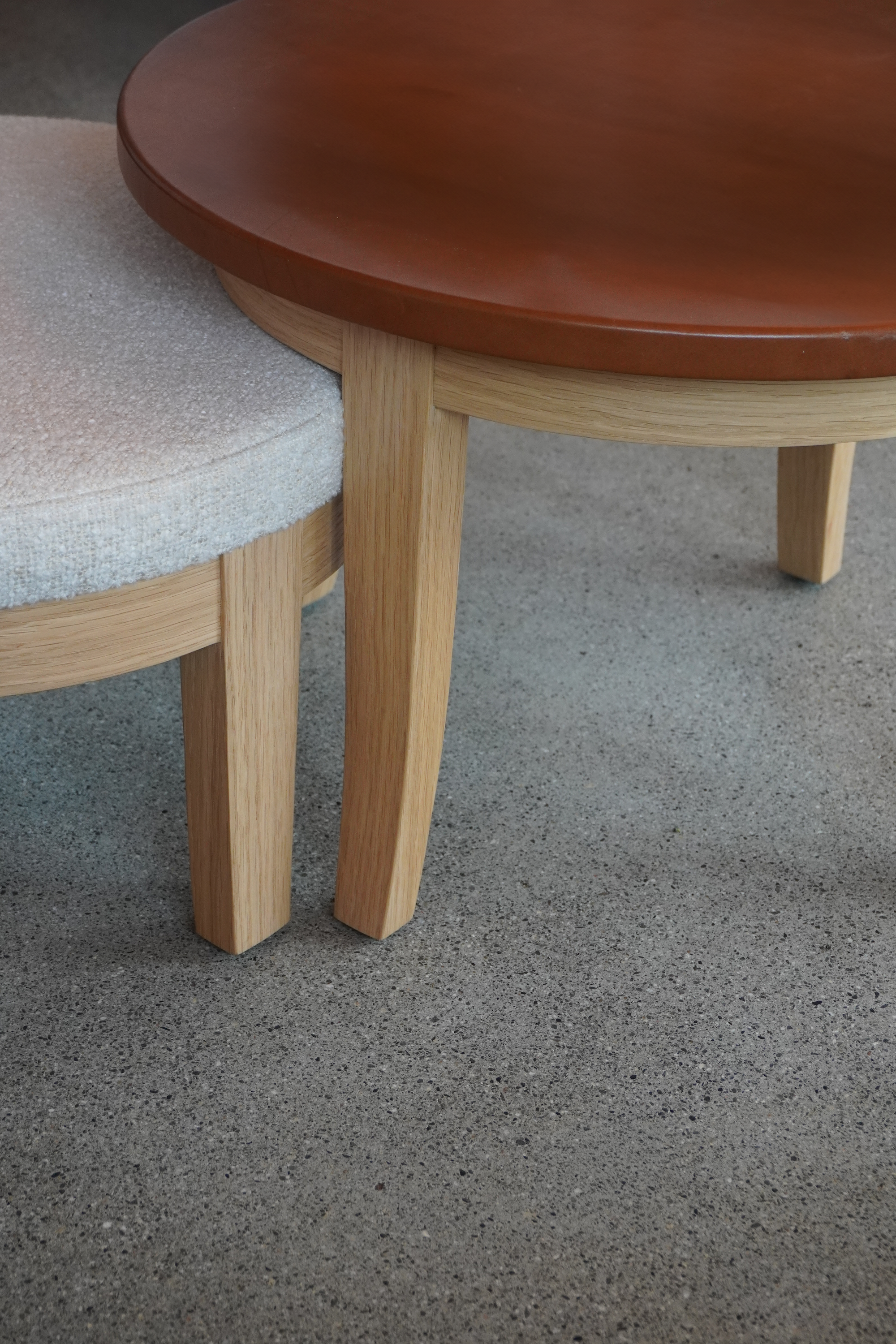 Nahaufnahme von zwei Holgstühlen mit unterschiedlichen Sitzflächen, eines mit hellen, das andere mit dunklen Holz, auf einem grauen Boden.