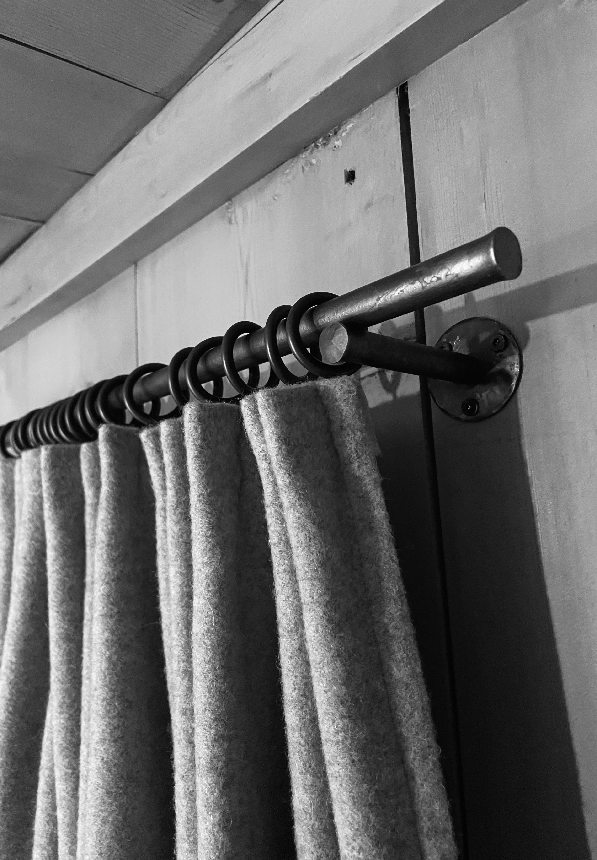 Grauer Vorhang an einem metalnen Gardinenstange vor einer Wand.
