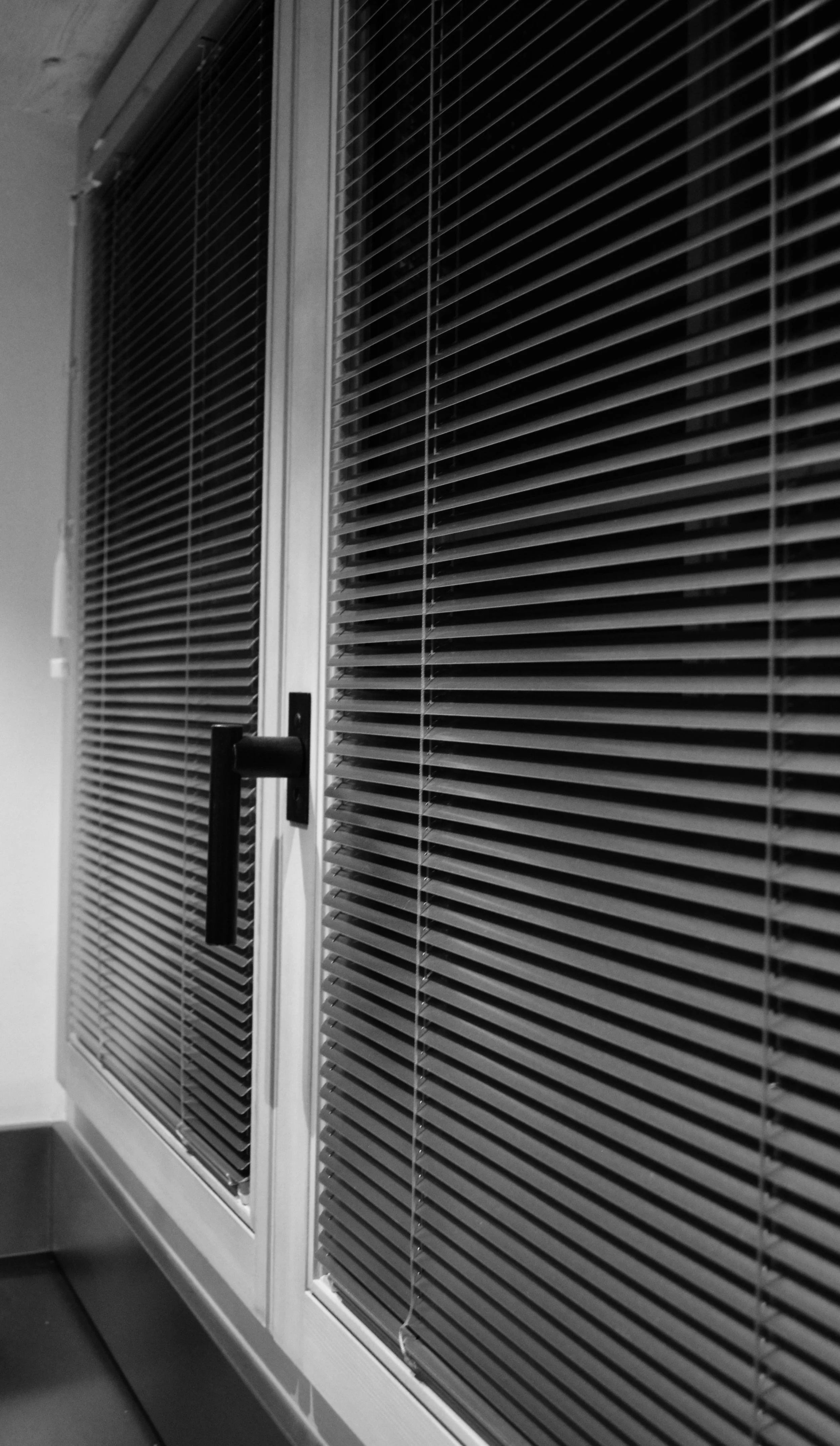 Ein Kühlschrank mit geschlossenen Jalousien, schwarzem Griff und weißem Rahmen, in einem Innenraum.